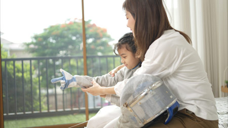 A girl in fencing gear with their mother preparing sports equipment before practicing fencing in...