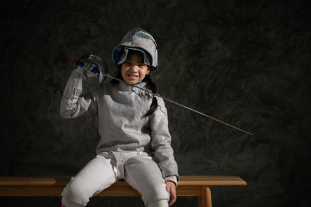 A girl in fencing gear sitting on a bench, ready for the Ã©pÃ©e competition