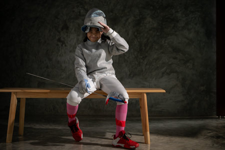 A girl in fencing gear sitting on a bench, ready for the Ã©pÃ©e competition