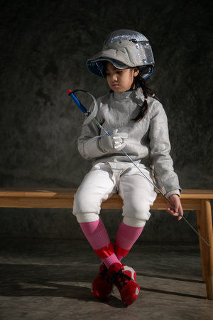 A girl in fencing gear sitting on a bench, ready for the Ã©pÃ©e competition