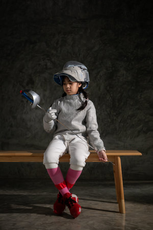 A girl in fencing gear sitting on a bench, ready for the Ã©pÃ©e competition
