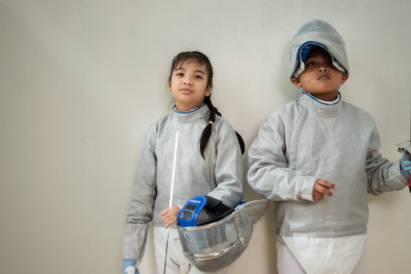 Before the tournament day, a boy and girl dressed in fencing gear are rehearsing in gym