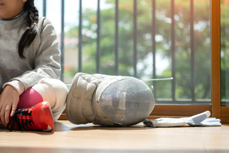 A girl in fencing gear resting before practicing fencing in preparation for the upcoming competition...