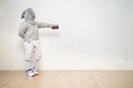Before the tournament day, a boy dressed in fencing gear are rehearsing in gym