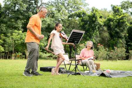 Happy Asian grandparents enjoying a picnic with their granddaughter in a green park, laughing and...