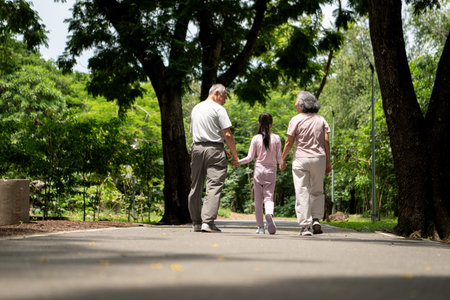 Happy Asian grandparents and granddaughter exercise joyfully together in a park, Active...