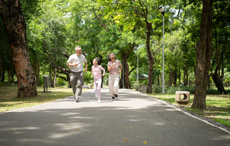 Happy Asian grandparents and granddaughter running joyfully together in a park, Active...