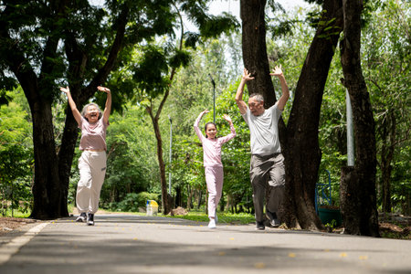 Happy Asian grandparents and granddaughter exercise joyfully together in a park, Active multigenerational family having fun outdoors in nature on a sunny dayの写真素材