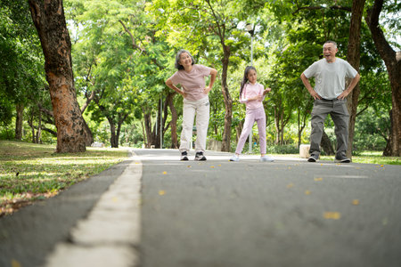Happy Asian grandparents and granddaughter exercise joyfully together in a park, Active...