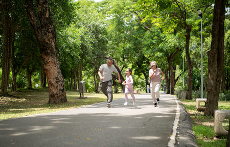 Happy Asian grandparents and granddaughter running joyfully together in a park, Active multigenerational family having fun outdoors in nature on a sunny dayの写真素材