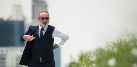 A senior businessman in a suit is walk in a hurry, with city buildings in the backgroundの写真素材