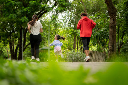 Asian family jogging together in the park. Parents and daughter exercising outdoors, promoting healthy lifestyle and family bondingの写真素材