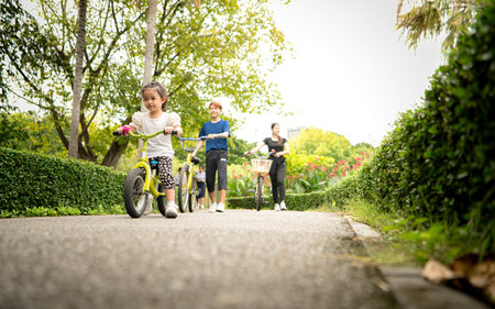 Parents and little girl to ride balance bike in park on the holidays of the week