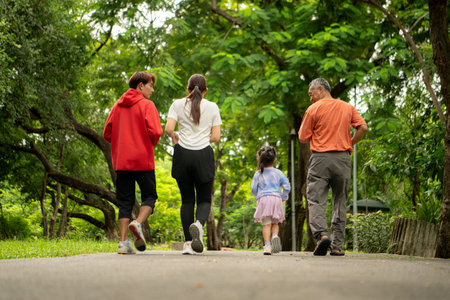 Asian family jogging together in the park. Parents, child, and grandfather exercising outdoors,...