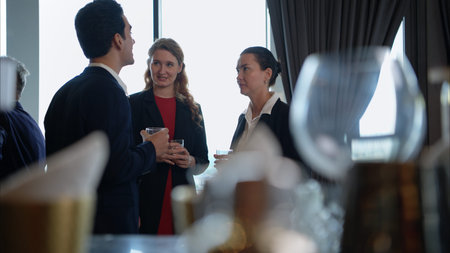 Business professionals networking and enjoying drinks at a corporate event in a modern office...