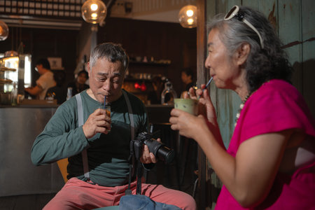 Senior couple enjoying coffee in a cozy cafe, smiling while looking at photos on a camera, symbolizing love, travel, and happy retirement lifestyleの写真素材