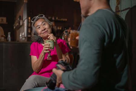 Senior couple enjoying coffee in a cozy cafe, smiling while looking at photos on a camera, symbolizing love, travel, and happy retirement lifestyleの写真素材