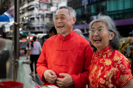 A happy senior couple strolls along a Chinatown in Bangkok, Thailand, holding hands and sightseeing together, enjoying travel and enjoying eating snacksの写真素材
