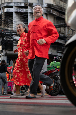 A happy senior couple strolls along a Chinatown in Bangkok, Thailand, holding hands and sightseeing together, enjoying travel and enjoying eating snacksの写真素材