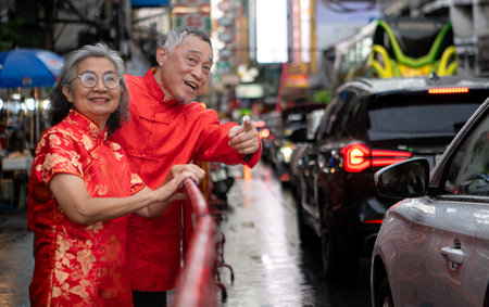 A happy senior couple strolls along a Chinatown in Bangkok, Thailand, holding hands and sightseeing together, enjoying travel and enjoying eating snacksの写真素材