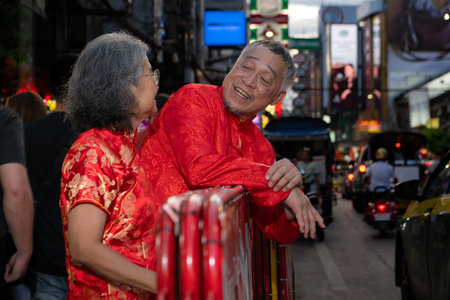 A happy senior couple strolls along a Chinatown in Bangkok, Thailand, holding hands and sightseeing together, enjoying travel and enjoying eating snacksの写真素材