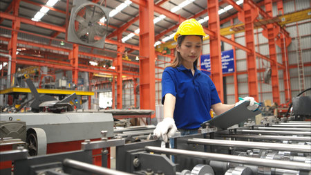 Young female worker inspecting machines on a production line with safety helmets and other equipment