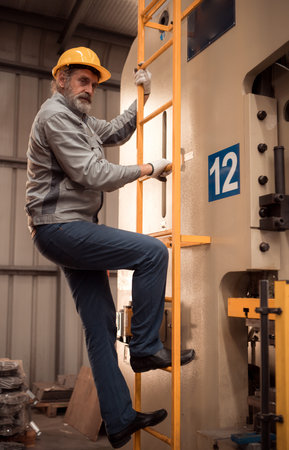 Senior experienced technician climbs a ladder to inspect and maintenance a large machine in metal sheet factoryの写真素材