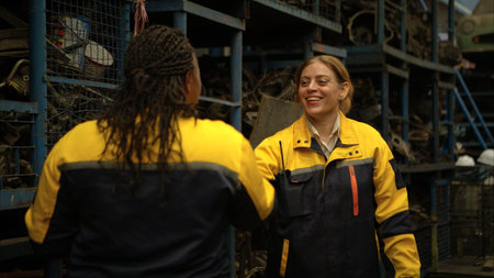 Two female engineers wearing safety gear inspecting car parts inventory in an industrial warehouse