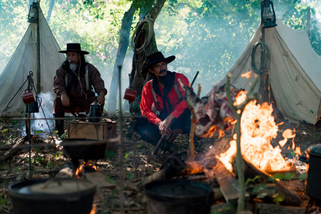 Group of cowboys preparing food at a campfire, roasting meat together in a warm and rustic outdoor settingの写真素材