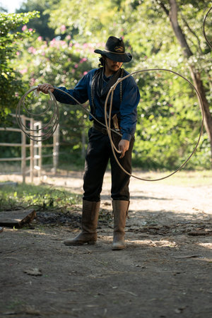 A cowboy handling a lasso rope for training at a rustic camp setup with wooden storage and cooking tools in the backgroundの写真素材