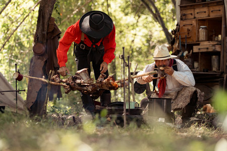 Two cowboys preparing food at a campfire, roasting meat together in a warm and rustic outdoor settingの写真素材