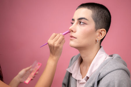 A makeup artist applying cosmetics to a woman with a buzz cut in a professional beauty studioの写真素材