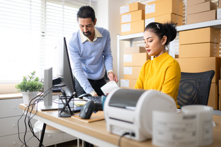 Business owner and employee labeling packages using printer and tablet in warehouse office