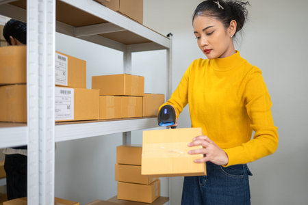 Female warehouse staff scanning barcode on cardboard box, managing inventory and order processing in...