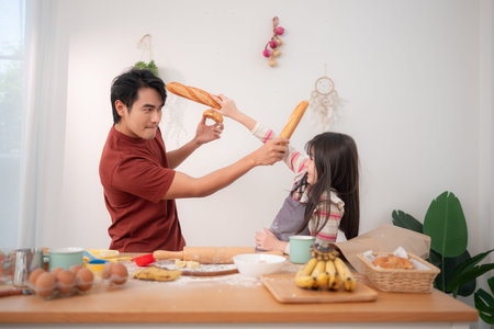 A father and daughter playfully sword-fight with baguettes in the kitchen, creating a fun and lively family cooking momentの写真素材