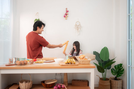 A father and daughter playfully sword-fight with baguettes in the kitchen, creating a fun and lively...