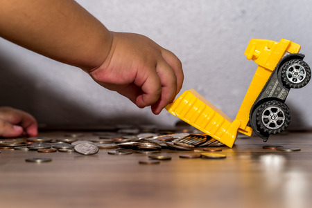 business and money concept -  hands of kid holding The truck pours out the coins of the bodyの写真素材