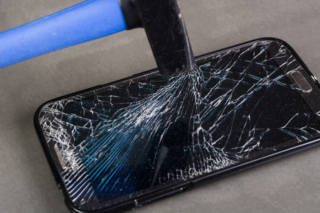 Smartphone with broken glass and hammer on gray backgroundの写真素材