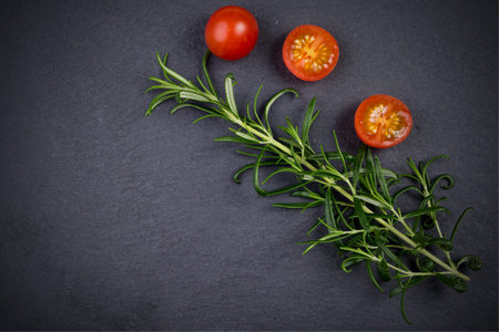 Fresh rosemary herb twig and tomatoes on black slate backgroundの写真素材