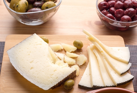 Spanish manchego cheese on wooden board with olivesの写真素材