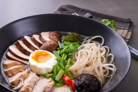 Japanese ramen soup with chicken, mushrooms, pasta, egg and chives on a black background