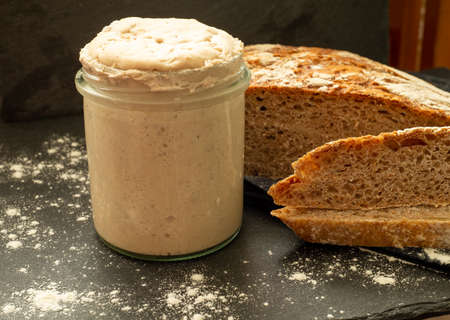 Homemade sourdough starter in glass on dark background and graham breadの写真素材