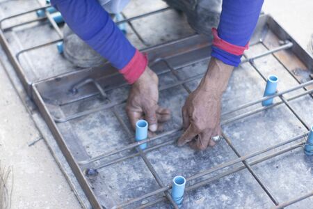 Workers are using steel pliers to clamp the wire in order to twist to fasten the blue PVC tube strand to the steel frame laid for making a pattern for making cement pipe caps.の写真素材