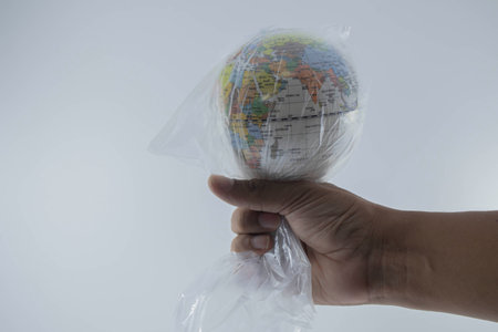 Globe is wrapped in plastic on hand of human . Show the environmental problem with the pollution of...