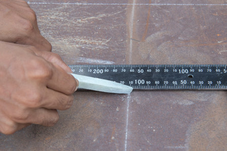 A white stone chalk positioned with yellow color measure tape is in the hands of workers. On a rusty...
