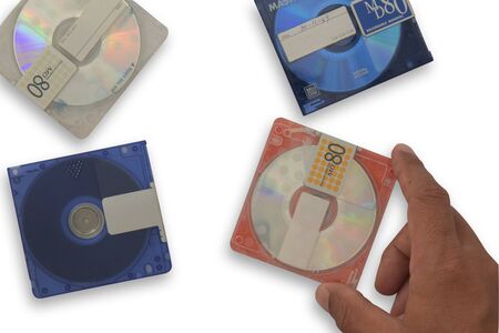 Isolate used Orange mini disc MD in right hand over other MDs. are scratches on the skin. Put on white background for data and music recording, Concept music players, high-capacity music discs, old rewritable data sheets  with clipping partsの写真素材