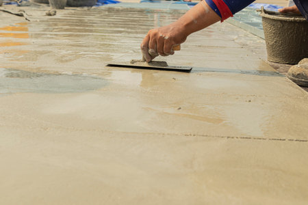 hand of worker holding steel trowel in hands on cement surface  for ground is being smoothed with ...