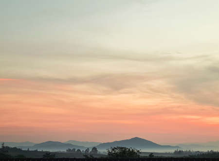 Morning blur over mountains and trees. The first and last light of the day in sky with beautiful red and yellow clouds sunlight as  background. have white fog around. concept village in mountain.の写真素材