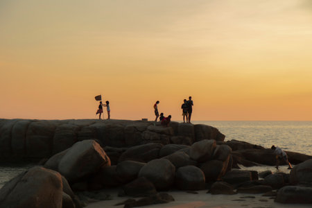 The stones on beach in evening have the background of the sea and the evening sun. There are people standing on rocks and flagsの写真素材