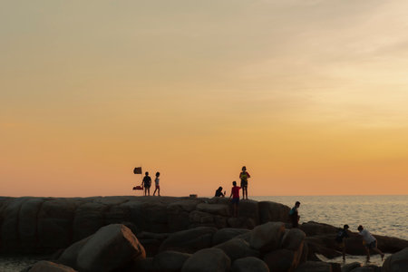 The stones on beach in evening have the background of the sea and the evening sun. There are people standing on rocks and flagsの写真素材